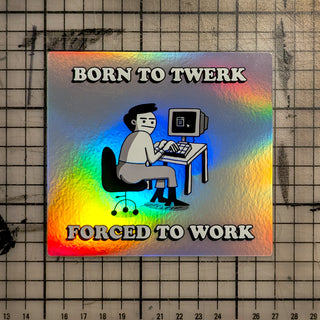 A holographic sticker featuring a cartoon office worker sitting at a retro computer desk with a computer monitor. Above the character, bold letters spell ‘BORN TO TWERK’, and below, ‘FORCED TO WORK’. The sticker has a rainbow iridescent finish that shimmers in the light, and is placed on a grid background for scale.