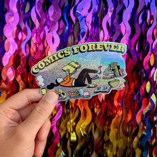 A hand holds a die-cut sticker featuring the text 'COMICS FOREVER' and an illustrated person surrounded by books and reading materials. The background is a vibrant, multicolored metallic tinsel curtain.