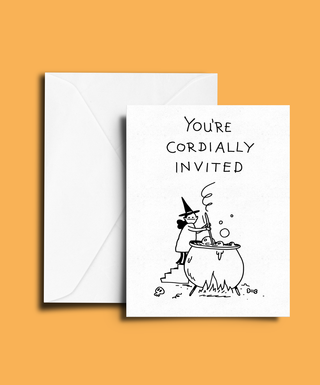A white greeting card with a black hand-drawn illustration of a witch stirring a cauldron and the text 'YOU'RE CORDIALLY INVITED', shown in front of a white envelope on a solid orange background.
