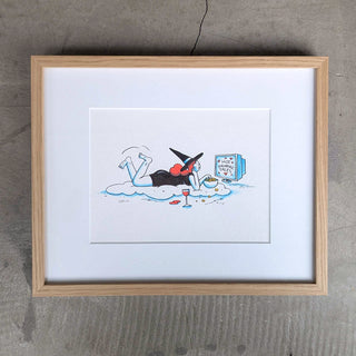 Framed illustration of a witch lying in front of a TV, wine glass, and book on a concrete floor.