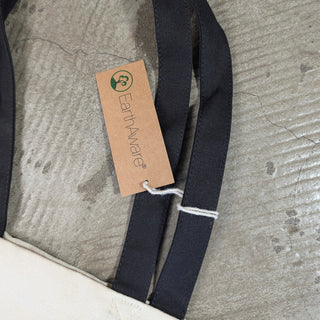 Close-up of a dark navy fabric strap with a kraft paper hangtag that reads EarthAwards, laid on a textured gray surface.