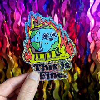 Artist-designed vinyl sticker with holographic glitter edges, depicting a sweating, fire-surrounded Earth and the deadpan ‘This is Fine.’ text.