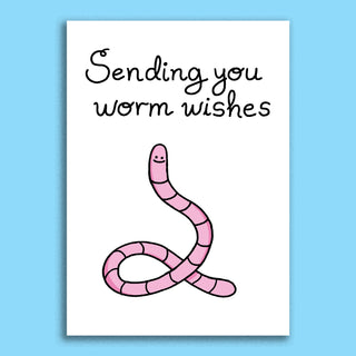Cute cartoon worm greeting card featuring a smiling pink worm and playful handwritten message 'Sending you worm wishes'. Ideal for quirky, funny, or lighthearted occasions. Blank inside for custom notes. Displayed with white envelope on blue background."